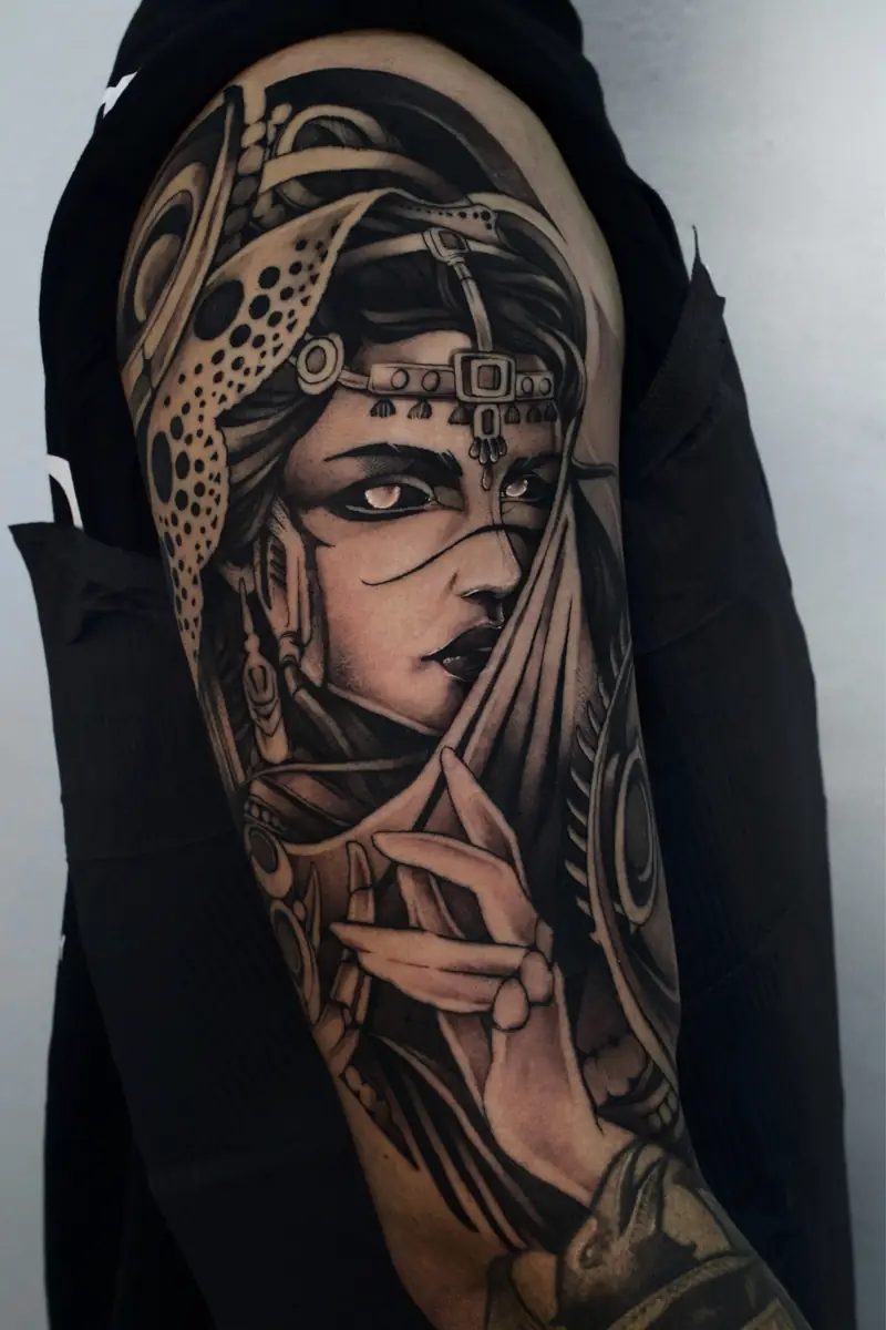 Vidente com véu sobre o rosto e tiara ornamentada, tatuada no braço
