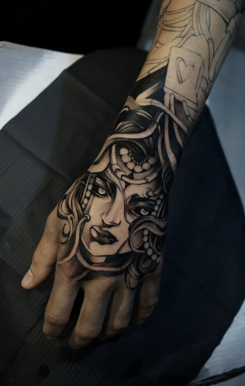 Medusa com cabelos de serpente e colares de pérolas, tatuada nas costas da mão
